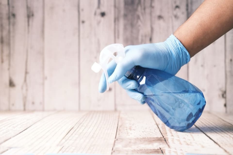 A gloved hand holding an unlabelled trigger spray bottle of cleaning solution