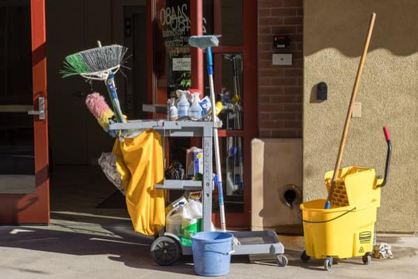 A loaded janitorial cart with brooms, bottles and a mop bucket