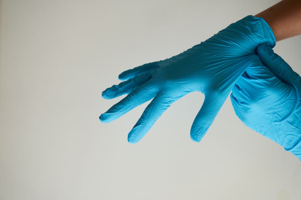 A pair of blue disposable nitrile gloves being pulled on