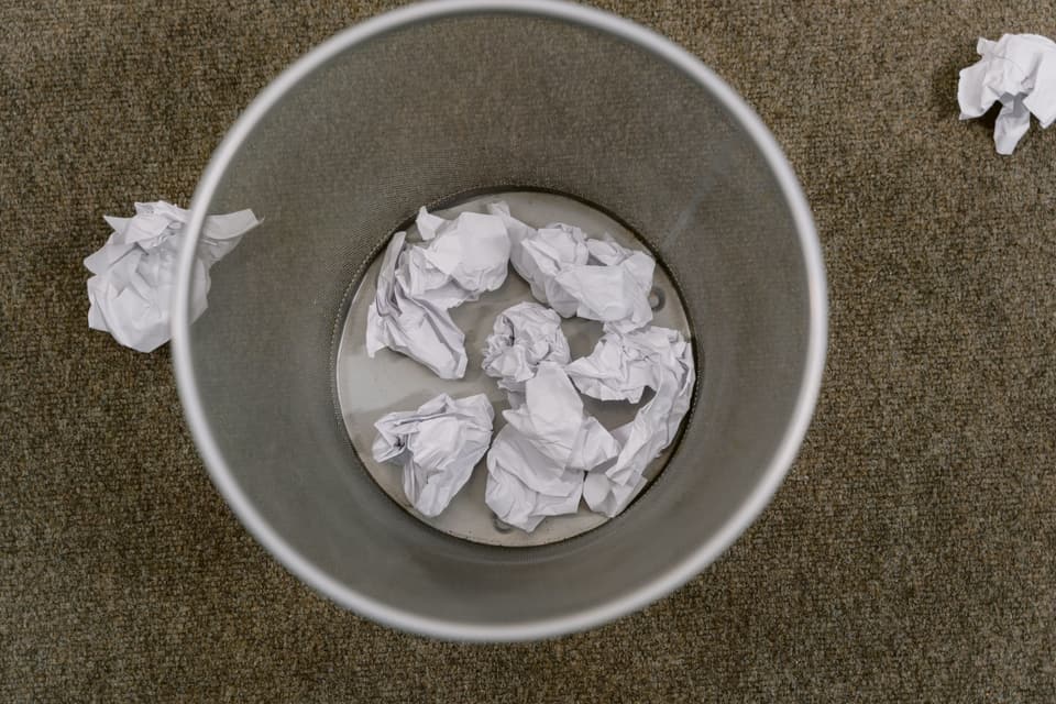 Looking down into an office waste bin part-filled with crumpled paper