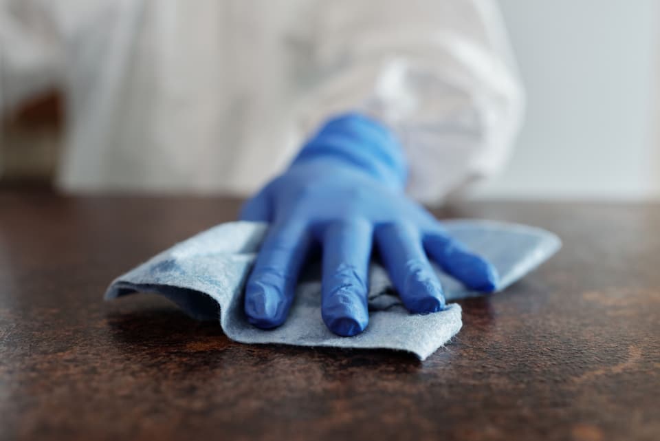 A gloved hand wiping a dark worktop with a folded cloth