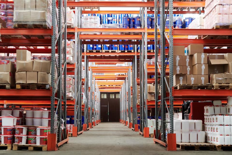 Pallets of cleaning chemicals, buckets and cartons on racking in a supply warehouse aisle