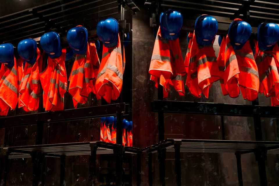 Rows of orange high-visibility vests and blue hard hats hanging on racks